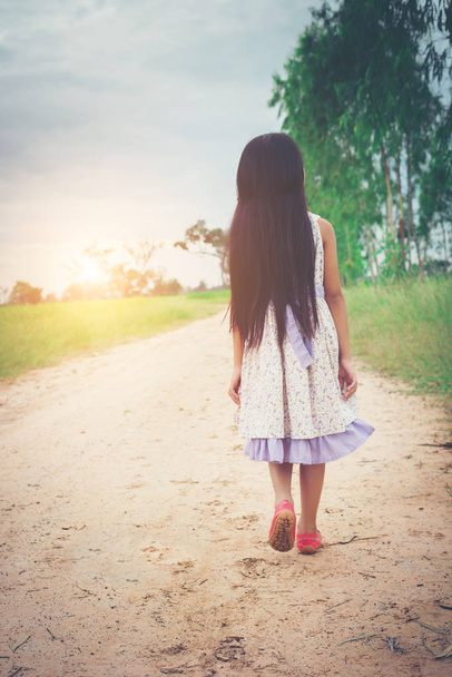 Little girl with long hair wearing dress is walking away from yo - Fotó, kép