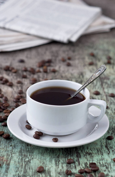 Чашка чорної кави на дерев'яний стіл з розкиданими зерна і газети. Чорна кава гарячий напій зерен газета дерев'яними тлі білого чашки сніданок - Фото, зображення
