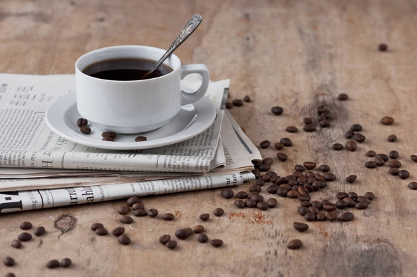 Una tazza di caffè nero su un tavolo di legno con grani sparsi e giornale. Caffè nero Bevanda calda cereali Giornale Fondo di legno Tazza bianca Colazione
 - Foto, immagini