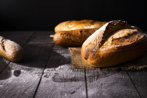 Bakery - gold rustic crusty loaves of bread and buns on black background. - Φωτογραφία, εικόνα