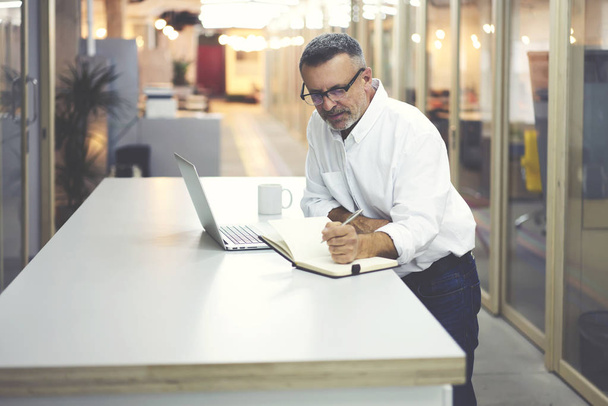 Опытный генеральный директор читает новости поиска информации на веб-сайтах с помощью ноутбука и Wi-Fi, опытный босс делает исследования и бухгалтерский учет для проверки продаж компании стоя в офисе
 - Фото, изображение