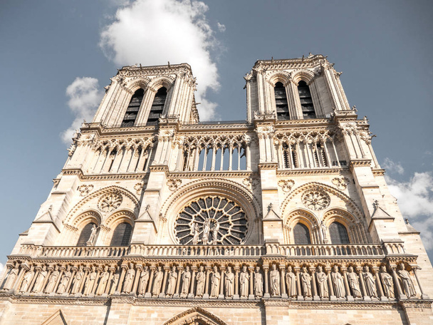 schönes touristisches Reisefoto mit Blick auf die Vorderfassade der weltberühmten und historischen gotischen Kathedrale Notre Dame in Paris Frankreich weiße Wolken am blauen Himmel darüber. - Foto, Bild