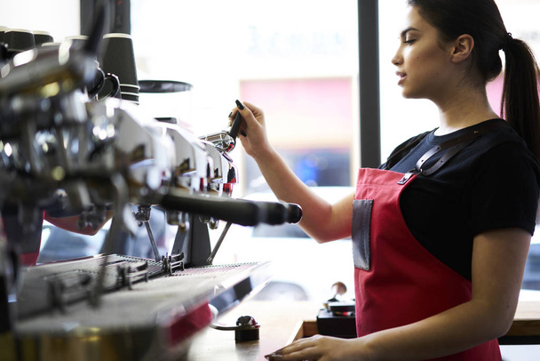 Cropped image of business female barista making tasty cappuccino on modern silver coffee machine.Female professional bartender preparing espresso on automatic metal appliance in coffee shop - Foto, immagini