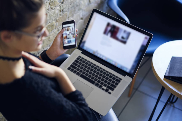 Обрізане зображення жінки, що тримає цифровий мобільний телефон в руці з порожньою зоною екрану, сидячи в приміщенні з сучасним ноутбуком, що підключається до високошвидкісного 4G Internet.Mock up простір для реклами
 - Фото, зображення