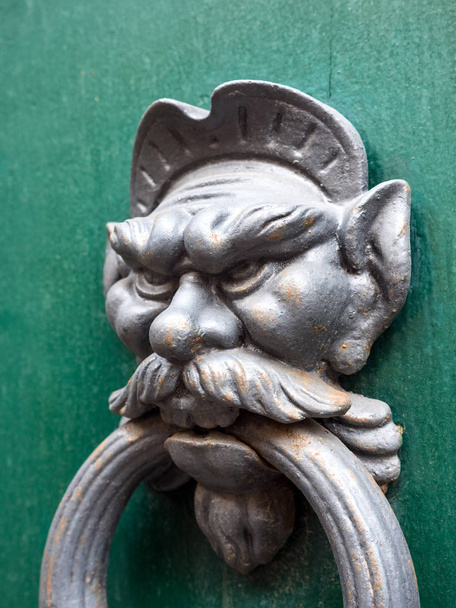 Funny, amusing or humorous close up photograph of a weathered metal antique door knocker caricature of a man with a mustache big ears and nose on a green painted wood door in Pisa Italy. - Photo, Image