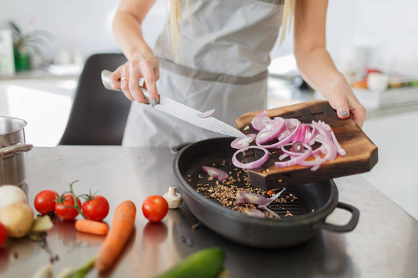 woman cut fresh red onion on a wooden board, cooking in the kitchen. The concept of  healthy food. - Фото, изображение