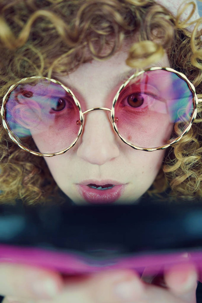Портрет молодой блондинке с вьющимися волосами в розовые очки, с помощью телефона - Фото, изображение