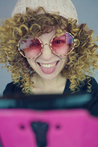 Portrét mladé blond ženy s kudrnatými vlasy v růžové brýle pomocí telefonu - Fotografie, Obrázek