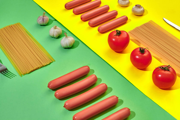 Sausages with tomatoes, mushrooms, spaghetti and garlic on a green and yellow minimal background. Flat lay. Top view. - Fotografie, Obrázek