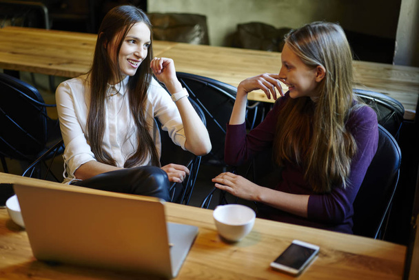 Beautiful young women having friendly conversation sitting at laptop computer in college interior during break.Hipster girls enjoying funny communication with each other sitting in coworking spac - Φωτογραφία, εικόνα