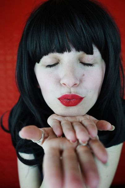 Портрет молодой женщины брюнетка с закрытыми глазами и ярко-красные губы на красном фоне - Фото, изображение