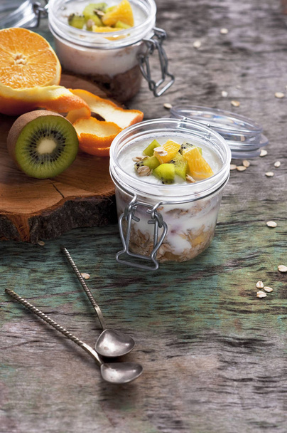 Yogurt per la colazione con muesli e arancia di kiwi alla frutta in un barattolo di vetro su fondo di legno. Prodotti sani per la colazione
 - Foto, immagini