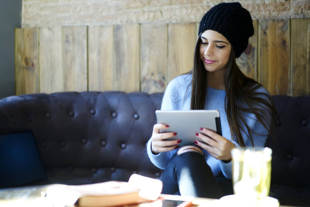 Tiivistetty hipster tyttö tyylikäs hattu selailu Internet-sivustoja ostoksia verkossa digitaalinen tabletti yhteyden nopea 4G internet istuu coworking tilaa mukava sohva
 - Valokuva, kuva