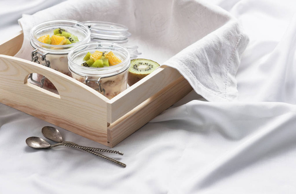 Здоровый завтрак из йогурта с мюсли и фруктами в стеклянной банке в лоток в постели. Здоровый завтрак
 - Фото, изображение