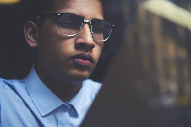 Cropped image of thoughtful hindu student in stylish optical eyeglasses carefully reading training book.Pensive male face of teenager in eyeglasses with black frame focused on literature - Zdjęcie, obraz