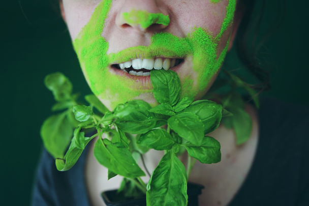 Ritratto di giovane donna con vernice verde sul viso con foglie fresche su priorità bassa vaga - Foto, immagini