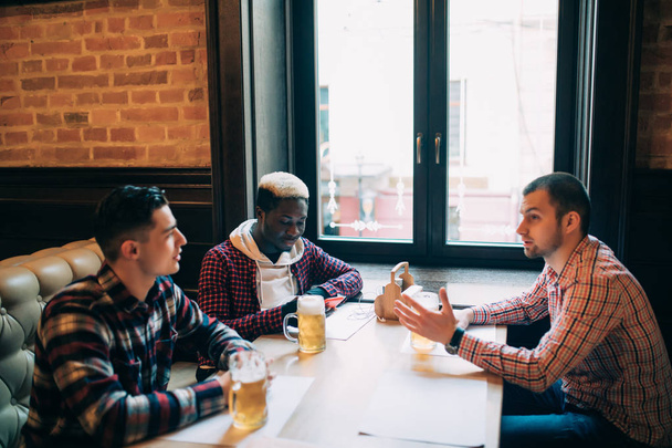 Multiraciale vrienden praten en drinken bier en rammelende brillen in pub - Foto, afbeelding