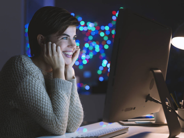 Happy smiling young woman connecting with her computer late at night, she is watching movies online - Foto, Bild
