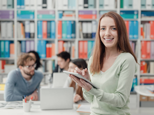 Smiling female student connecting with a digital tablet and group of students in the background - Foto, Bild