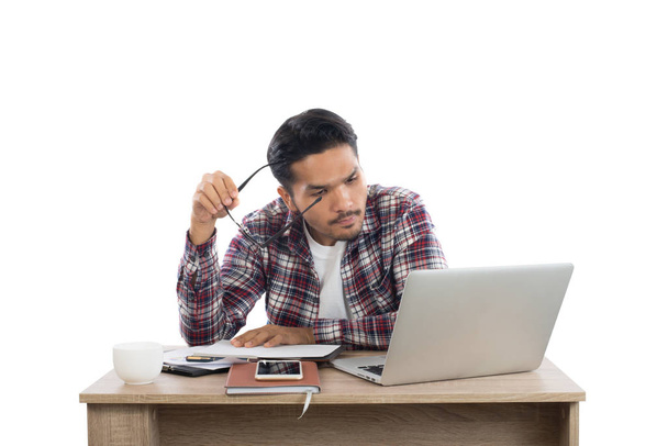 Задумчивый молодой человек, держащий очки и смотрящий на ноутбук
 - Фото, изображение