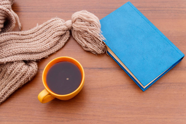Φλιτζάνι καφέ, πλεκτό κασκόλ και βιβλίο σε φόντο ξύλινη - Φωτογραφία, εικόνα
