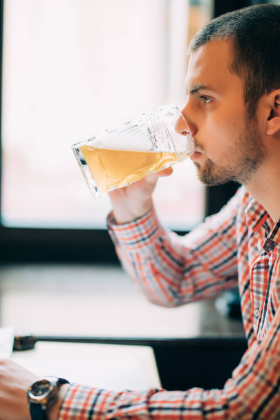 Man drinking beer. Side view of handsome young man drinking beer while sitting at the bar counter - 写真・画像