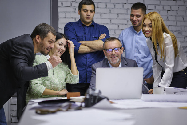 lächelnde männliche und weibliche Kollegen Designer im Büro tragen eine neue lustige Grafik auf einem modernen Laptop, der sich mit drahtlosem High-Speed-Internet verbindet und während der Konferenz am Besprechungstisch sitzt - Foto, Bild