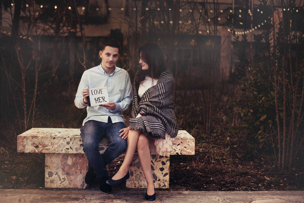 Couple sitting on a bench. Boyfriend holding note I Love Her - Fotoğraf, Görsel