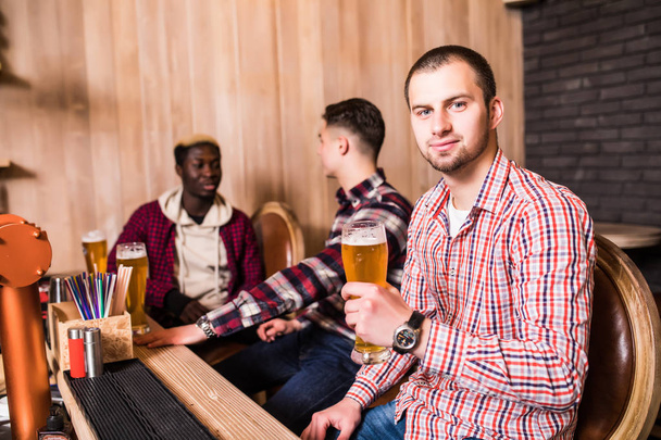 Mann trinkt Bier vor zwei trinkenden Freunden an Kneipentresen. - Foto, Bild