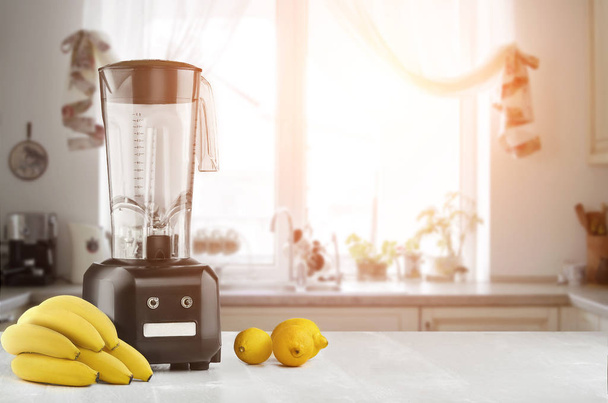 Metal food blender close-up with fresh exotic tropic fruits next to it on kitchen background with empty space. Sun flare - Photo, Image