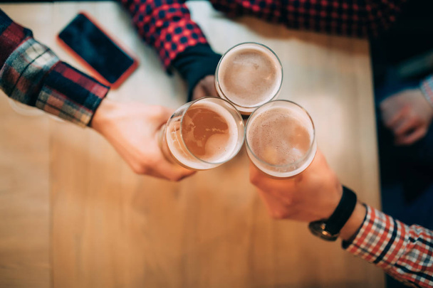 Um brinde. Close-up vista superior de amigos segurando canecas com cerveja
 - Foto, Imagem