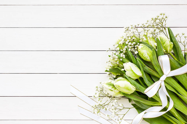 Букет з білих тюльпанів і гіпсофіли, прикрашений стрічкою на білому дерев'яному фоні. Вид зверху, простір для копіювання
 - Фото, зображення