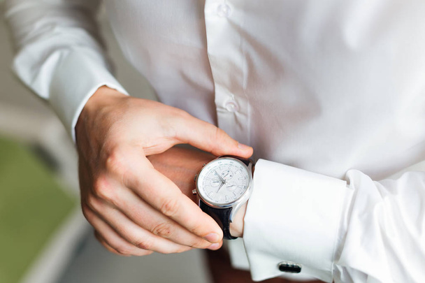 The fiance in a white shirt looks at the dial of wrist watch - Foto, afbeelding