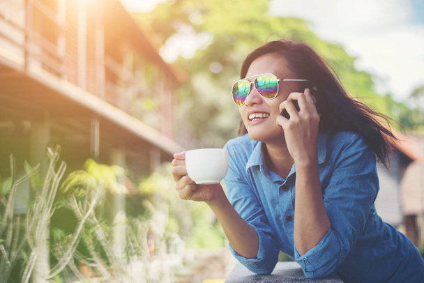 Fiatal csípő nő beszél telefonon, miközben egy csésze kávé  - Fotó, kép