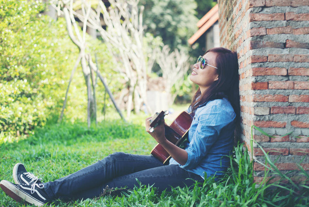 Joven chica hipster sentada tocando una guitarra y cantando
. - Foto, Imagen
