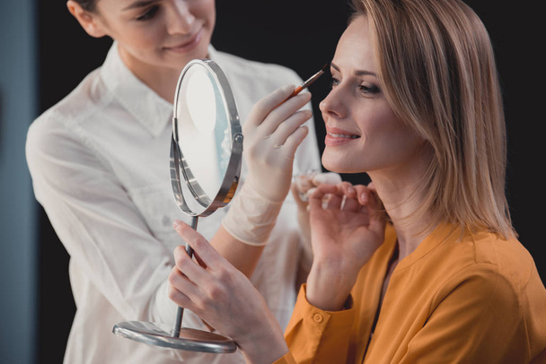 Outgoing cosmetologist creating make-up for beaming visitor - Valokuva, kuva