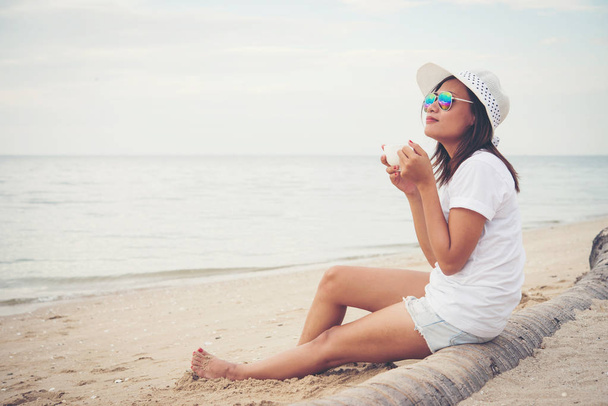 Beautiful young woman with coffee in hands sitting on the beach  - Photo, Image