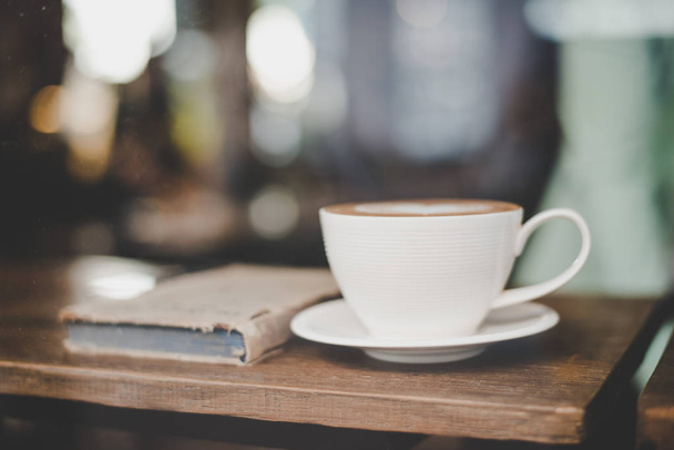 Cup of coffee with book in coffee shop vintage color blurred caf - Fotó, kép