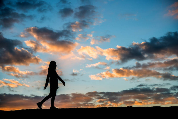 Sylwetka kobiety chodzenia o zachodzie słońca. - Zdjęcie, obraz