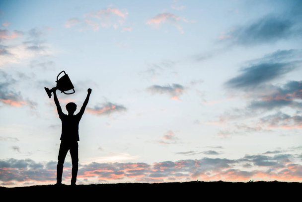 Silhouette man holding up a gold trophy cup. - Φωτογραφία, εικόνα