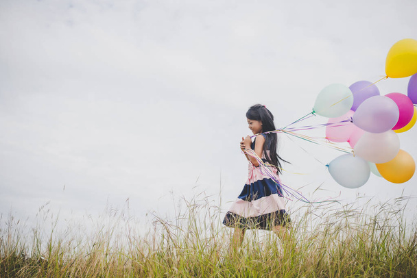 Pieni tyttö leikkii ilmapalloilla niityillä
. - Valokuva, kuva