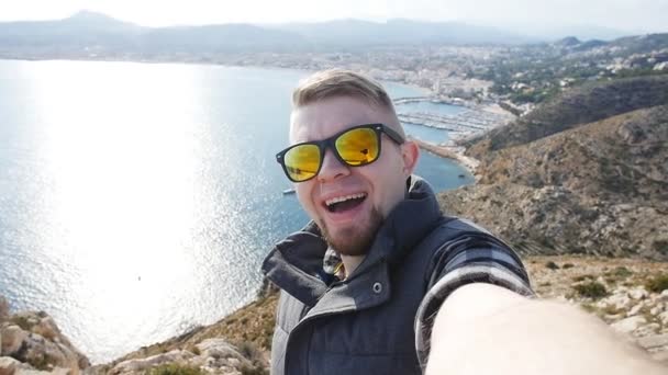 Mladík bere cestování selfie na pěší výlet den. Na pozadí moře a skály - Záběry, video
