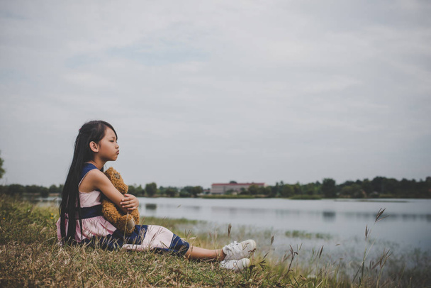 Ayısının meadows sahasında üzmek ile oturan küçük kız. - Fotoğraf, Görsel