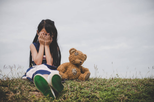 Μικρό κορίτσι να κάθεται με την αρκούδα αναστατωμένος στο meadows field. - Φωτογραφία, εικόνα