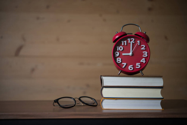 Alarm clock at 9am on stack of books with glasses on wooden table. Education concept.  - Fotó, kép