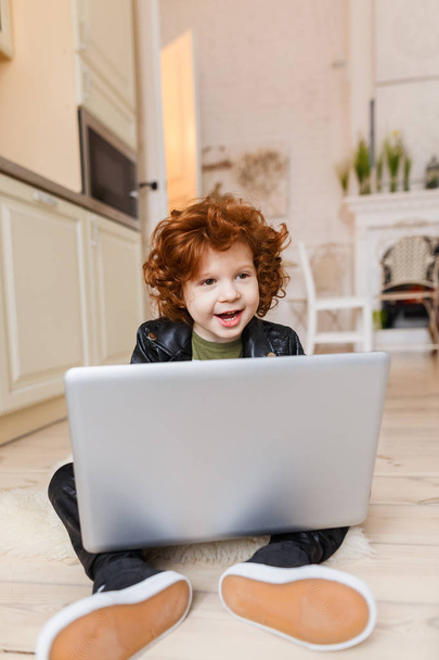 Little redhead boy uses a laptop - Fotó, kép