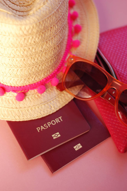 Nyári kiegészítők, szalma kalap, rózsaszín szalag, fürdőruha, napszemüveg, útlevél, több mint rózsaszín háttér. Utazás. Holliday. - Fotó, kép
