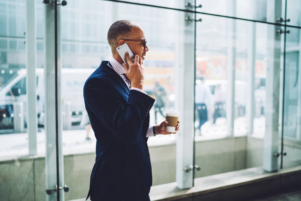 Confident man proud CEO in formal wear having mobile phone conversation about business during coffee break, skilled male entrepreneur lawyer talking on smartphone standing outdoors in city downtown - 写真・画像