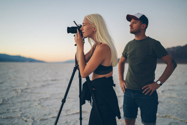 Male and female travelers taking picture of nature environment during evening dusk in Death valley, bloggers working together on shooting landscape of dry lake in Badwater having expedition together - 写真・画像