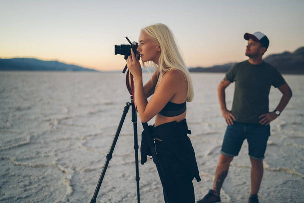 Young male and female travelers taking picture of scenic landscape in evening having journey together, female photographer making photo on digital camera beigh in expedition with boyfriend in Badwater - Photo, image